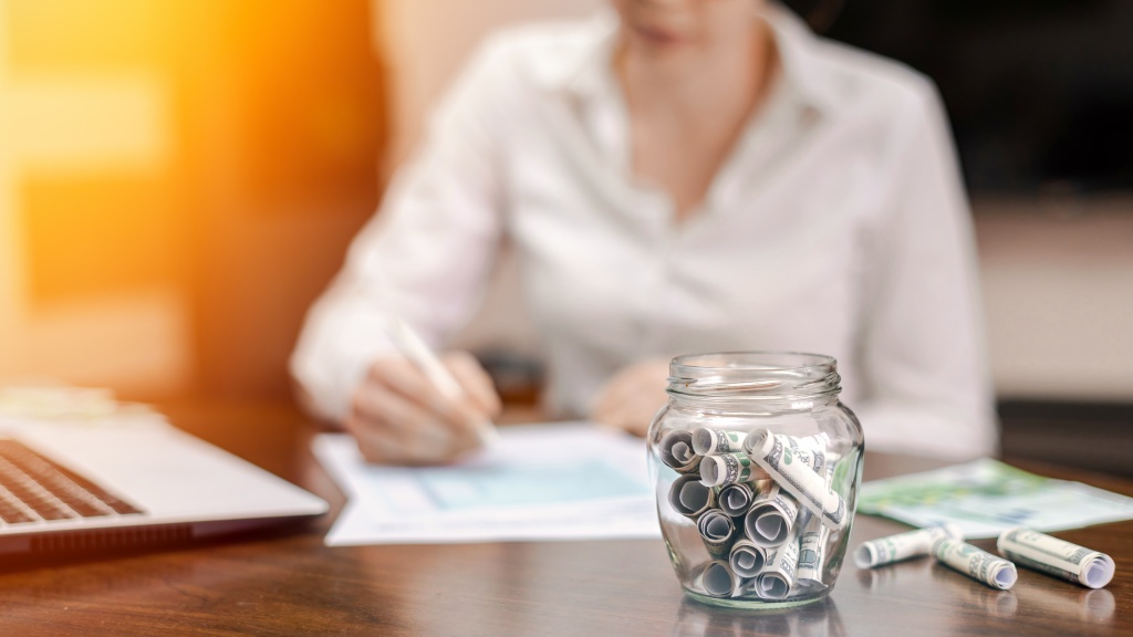 jar-with-rolled-banknotes-table-laptop-papers-woman-background.jpg деньги
