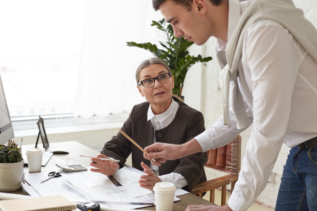 cropped-view-talented-ambitious-young-man-architect-holding-pencil-pointing-drawings-desk-while-showing-construction-project-his-senior-woman-boss-glasses-working-team.jpg совещание